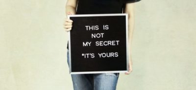 Woman holding a board with the words, this is not my secret, its yours.
