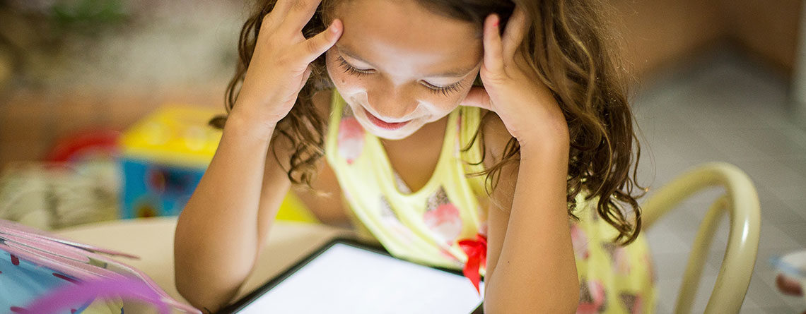 Child sat at desk online on a tablet.