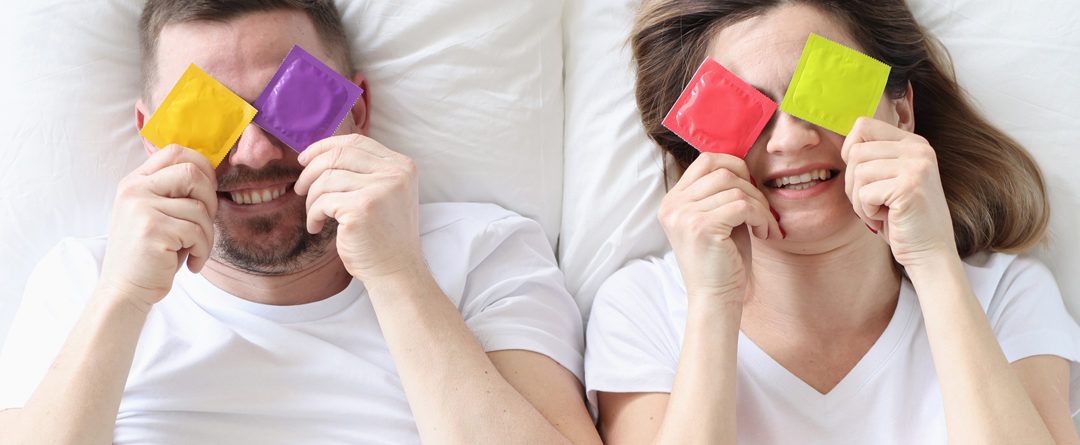 Couple hold condoms up and cover their eyes.