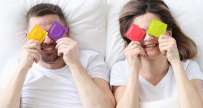 Couple hold condoms up and cover their eyes.