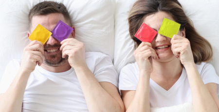 Couple hold condoms up and cover their eyes.