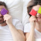 Couple hold condoms up and cover their eyes.